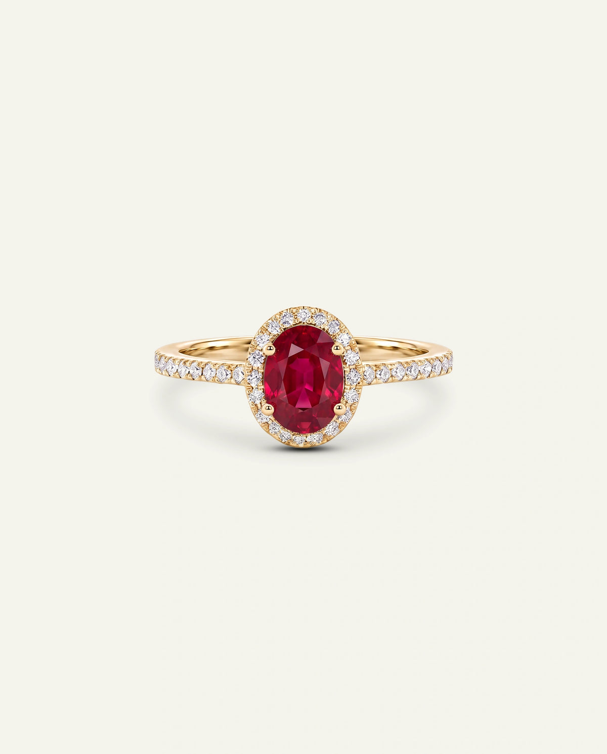 A yellow gold ring featuring an oval-cut red ruby center stone surrounded by a halo of small clear stones, with a pavÃ©-set gold band, shown on a light cream background.