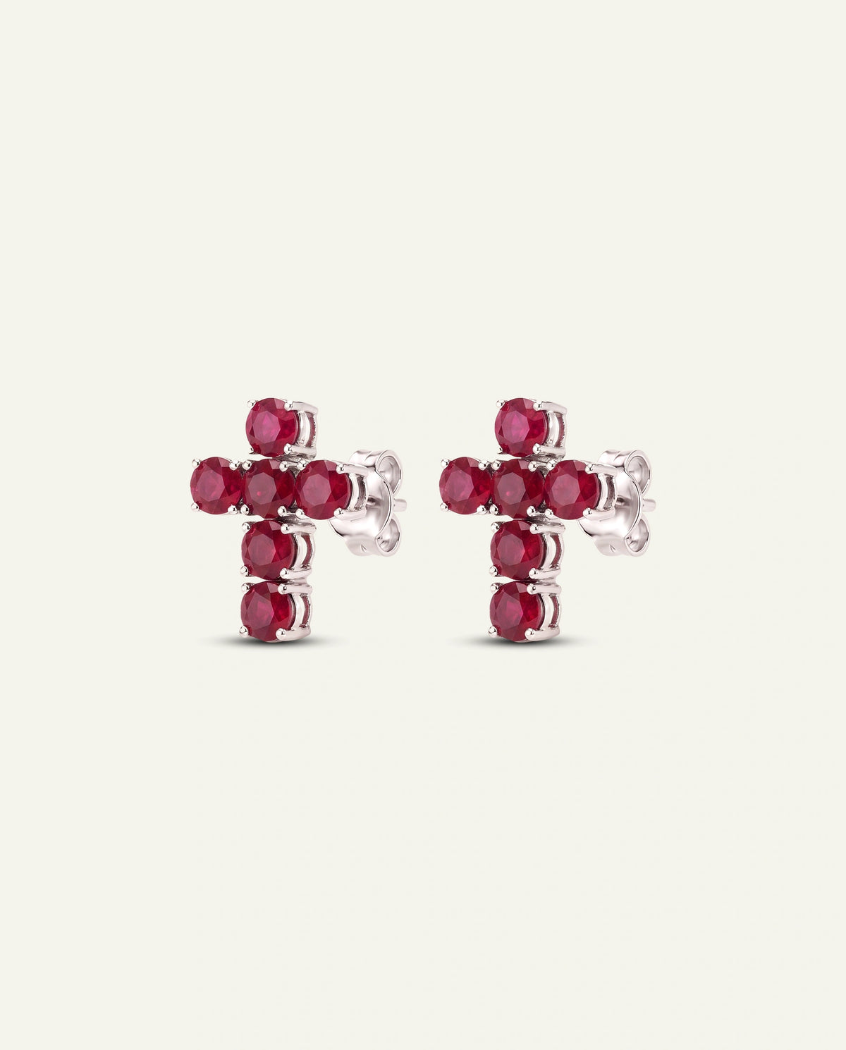 A pair of silver-toned cross stud earrings set with round red gemstones, shown against a plain off-white background.