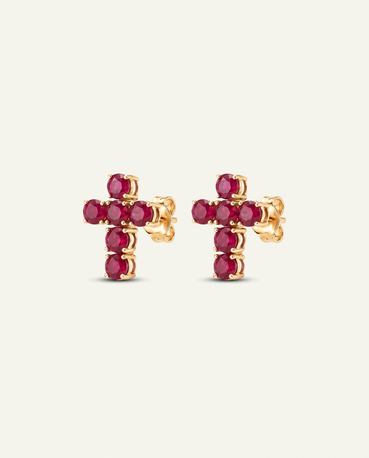 A pair of gold cross stud earrings set with round red gemstones, shown against a plain off-white background.