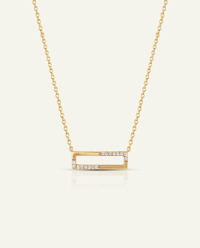 A gold open-bar necklace with a delicate chain and small clear stones set along the front edges of the bar, displayed on a light cream background.