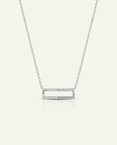 A silver-toned open rectangular bar necklace with a row of small clear stones on the right side, suspended from a delicate chain against a light cream background. - alternate view