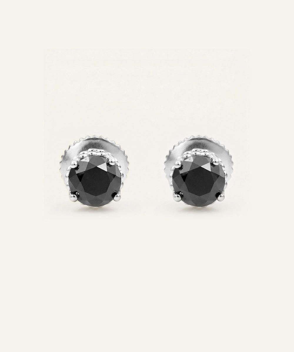 A pair of silver stud earrings with faceted black gemstones in a prong setting, shown against a plain off-white background.