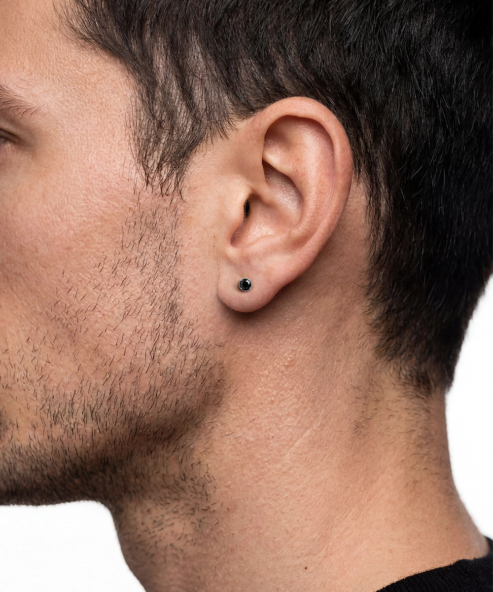 Close-up side profile of a man's head showing a small round stud earring in a dark metal setting on his earlobe.