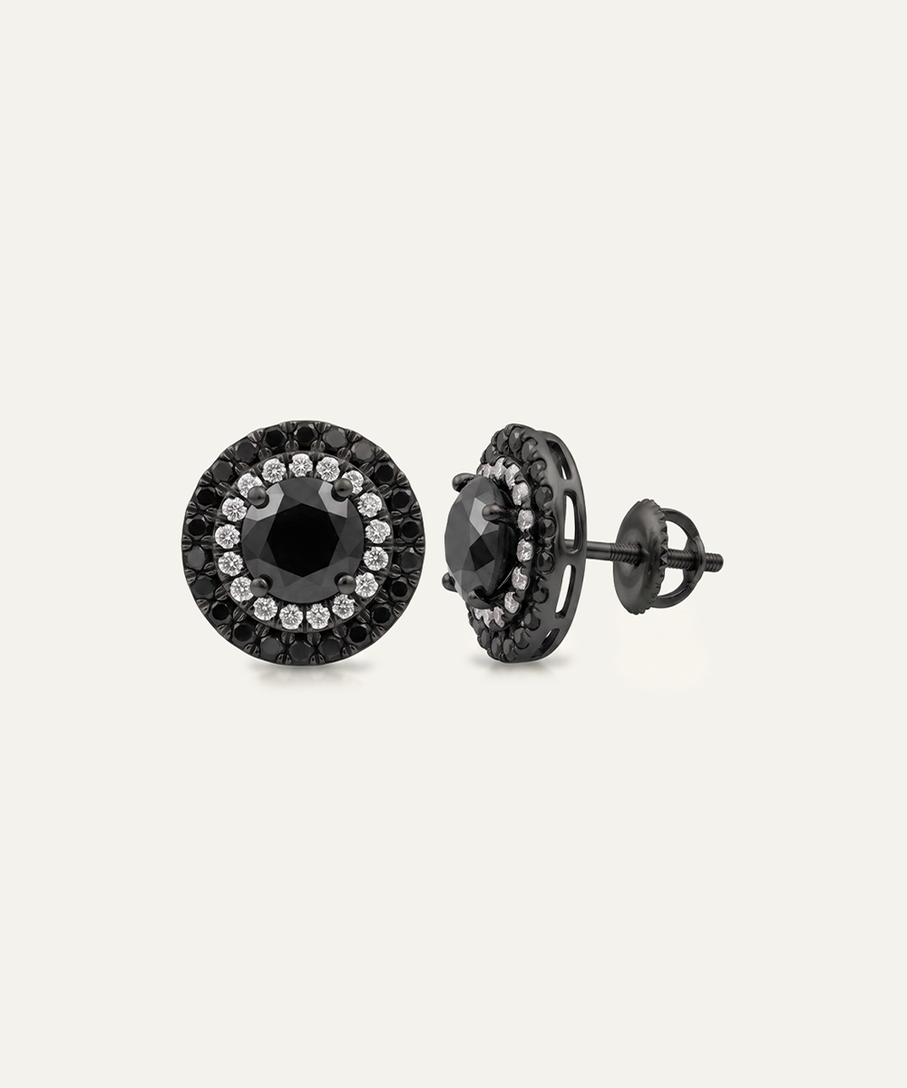 A pair of round black stud earrings with a halo design featuring small clear stones around a central black stone, shown on a light beige background.