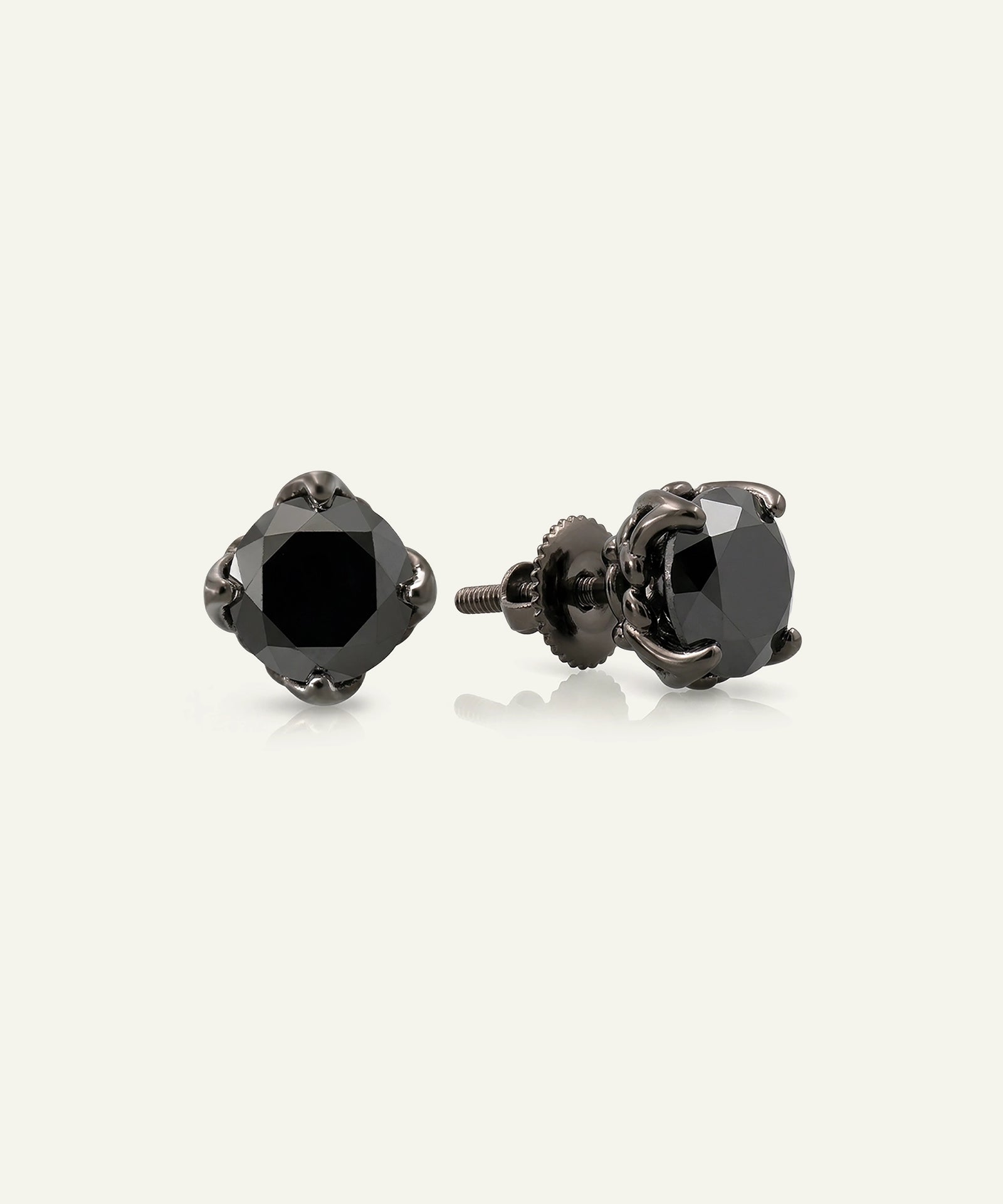 A pair of dark gunmetal stud earrings with faceted black gemstones, shown from front and side angles on a light cream background.