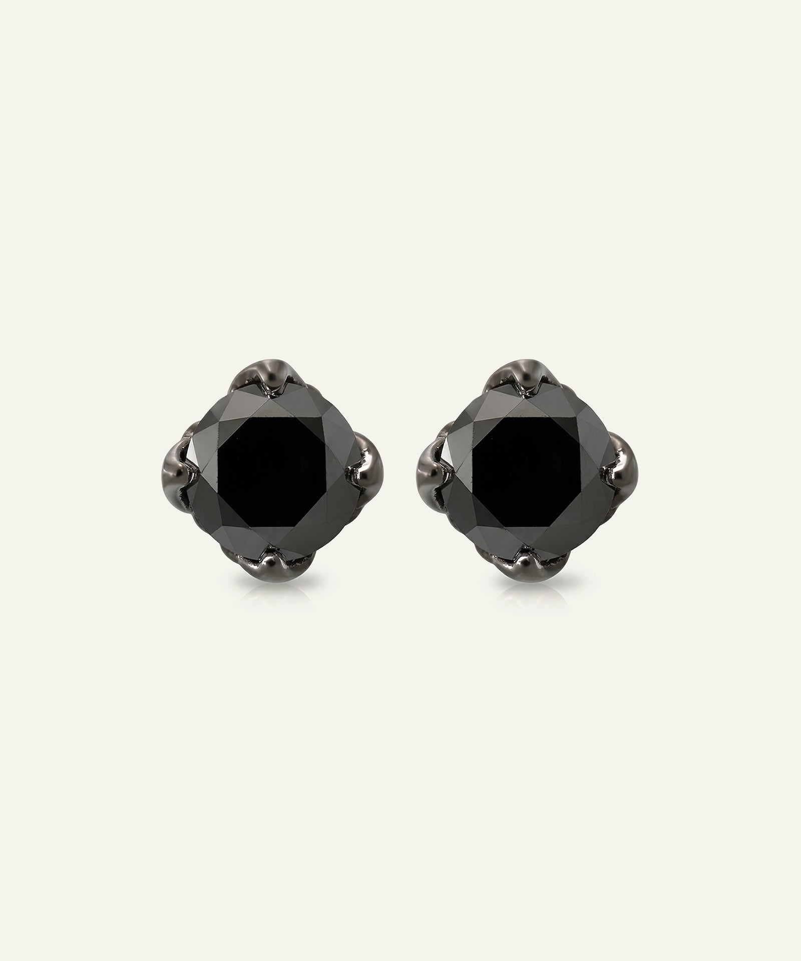 A pair of black faceted stud earrings with a central black gemstone and dark metallic settings, displayed on a light off-white background.