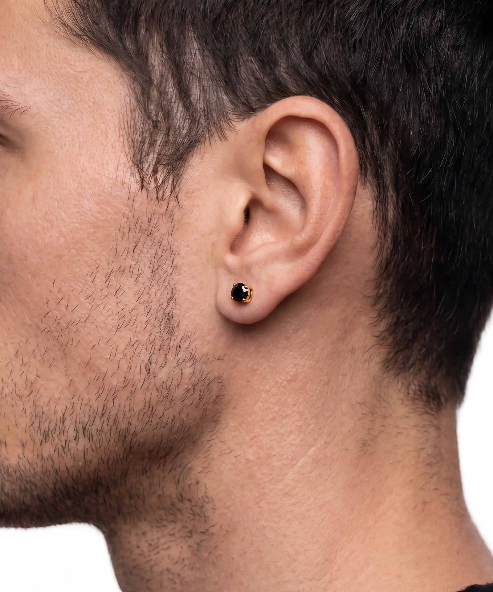 A close-up side profile of a man's head showing a small gold stud earring with a black circular stone set in his earlobe.