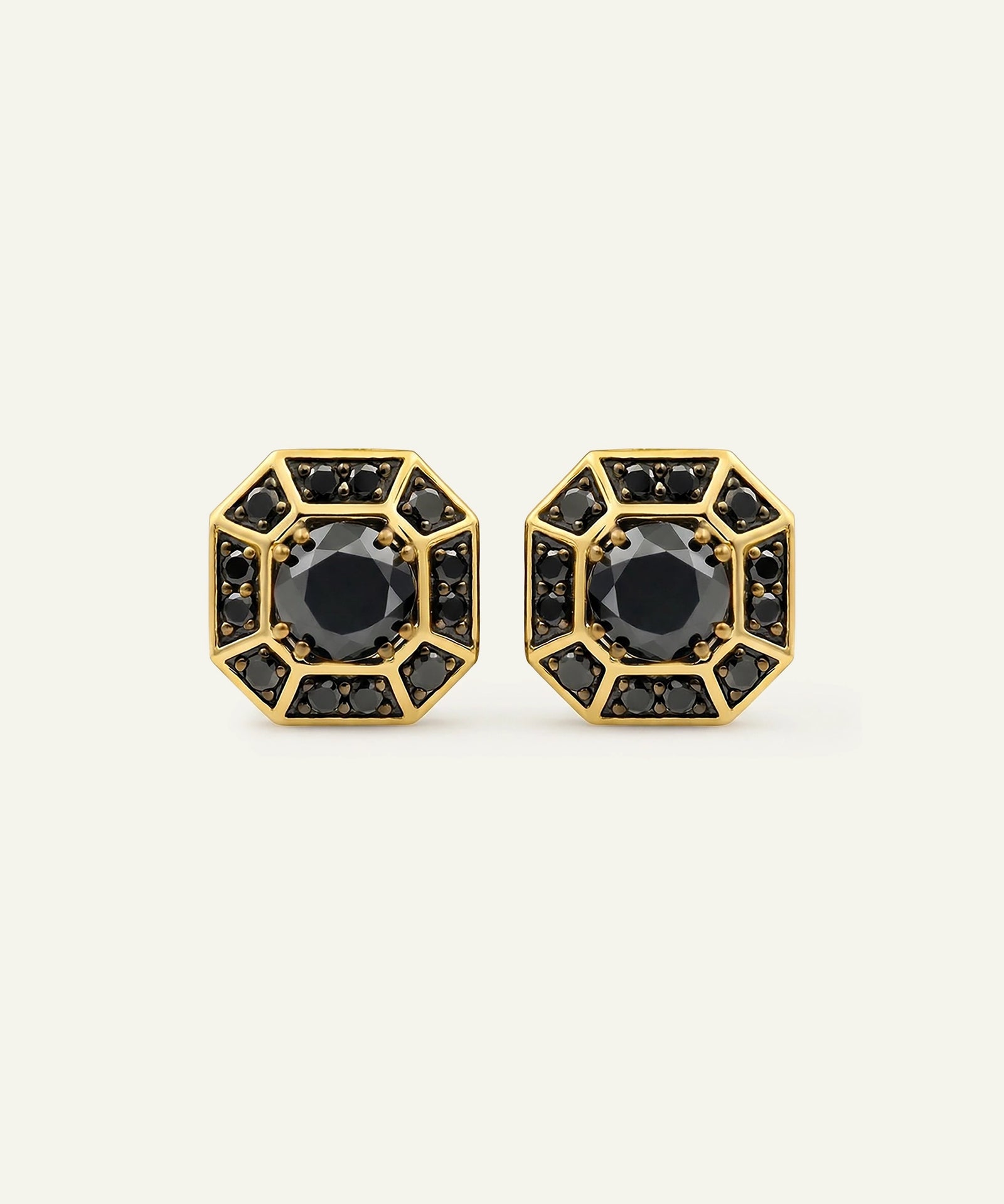 A pair of gold geometric stud earrings with black gemstone accents, displayed on a light cream background.