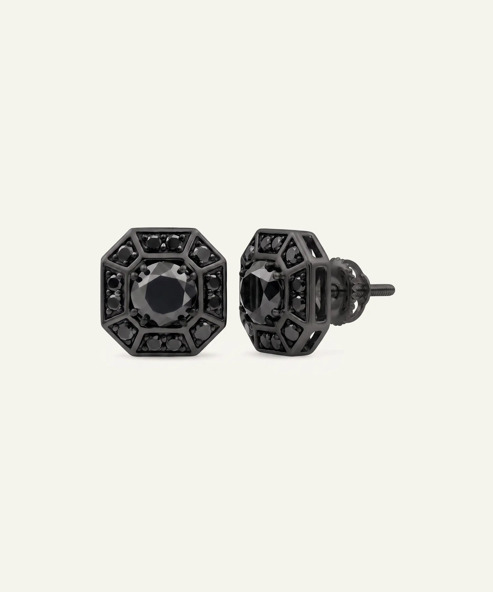 A pair of black geometric stud earrings with faceted octagonal shapes and central round black stones, shown on a light cream background.