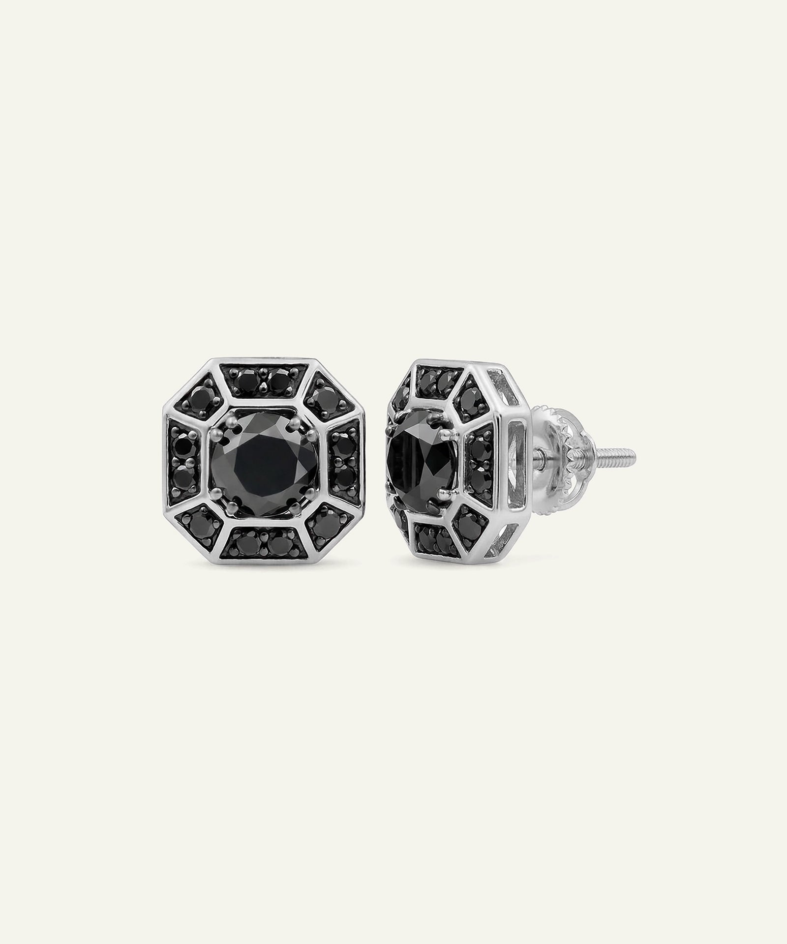 A pair of silver-toned geometric stud earrings with black stones, shown from both front and side angles on a light cream background.