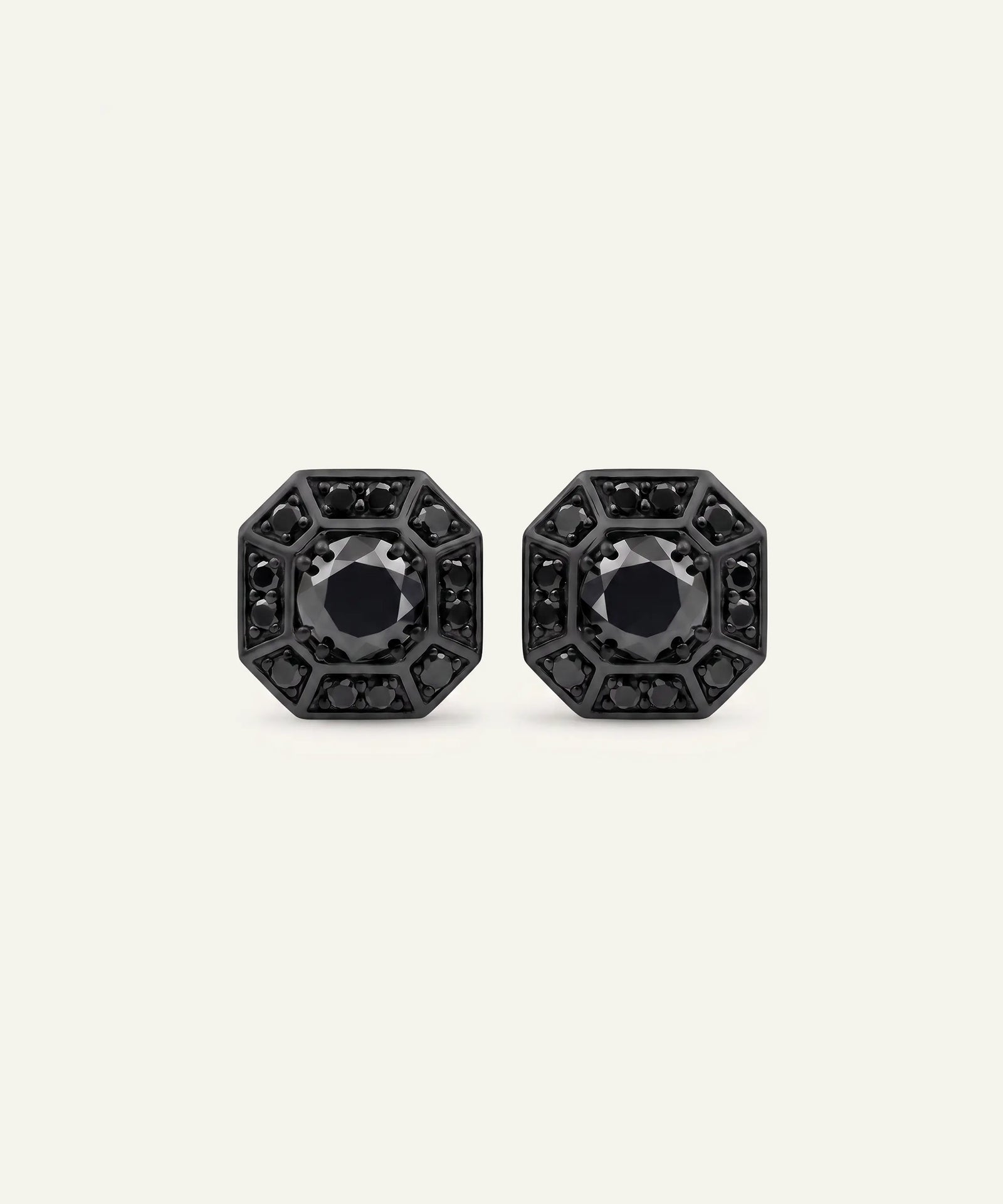 A pair of black geometric stud earrings with circular black centers and surrounding openwork details, displayed on a light cream background.