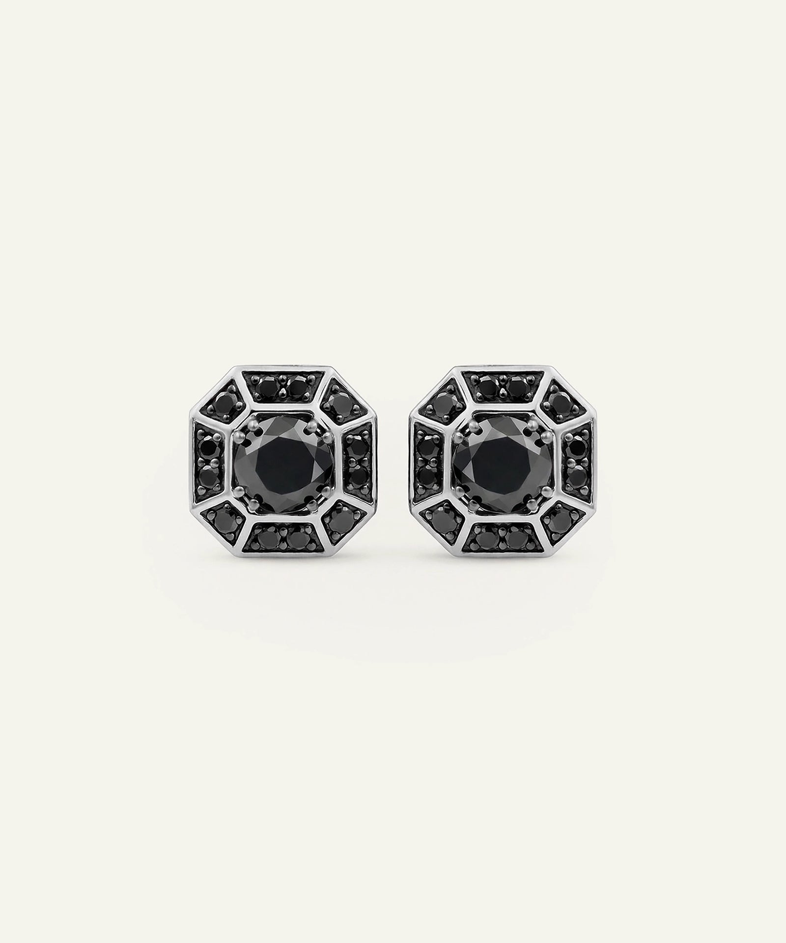 A pair of geometric stud earrings with black gemstones and silver-toned metal settings, displayed on a light cream background.
