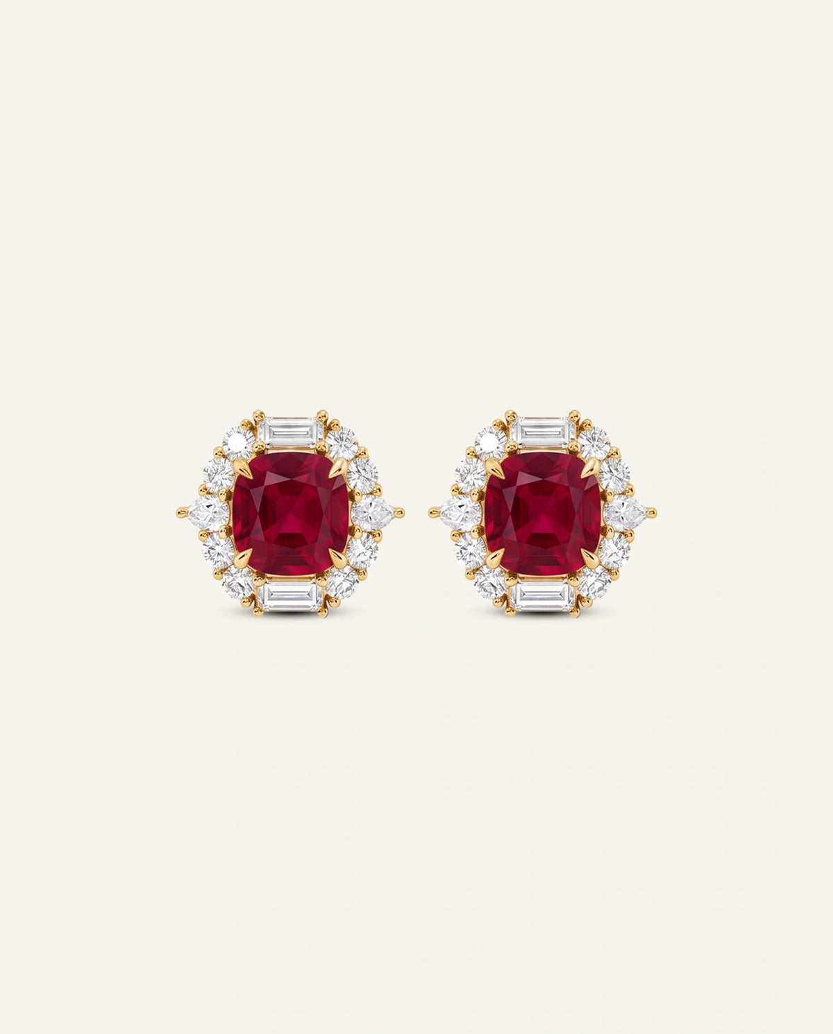 A pair of yellow gold stud earrings featuring cushion-cut red ruby centers surrounded by round and baguette-cut clear diamonds, set against a solid off-white background.