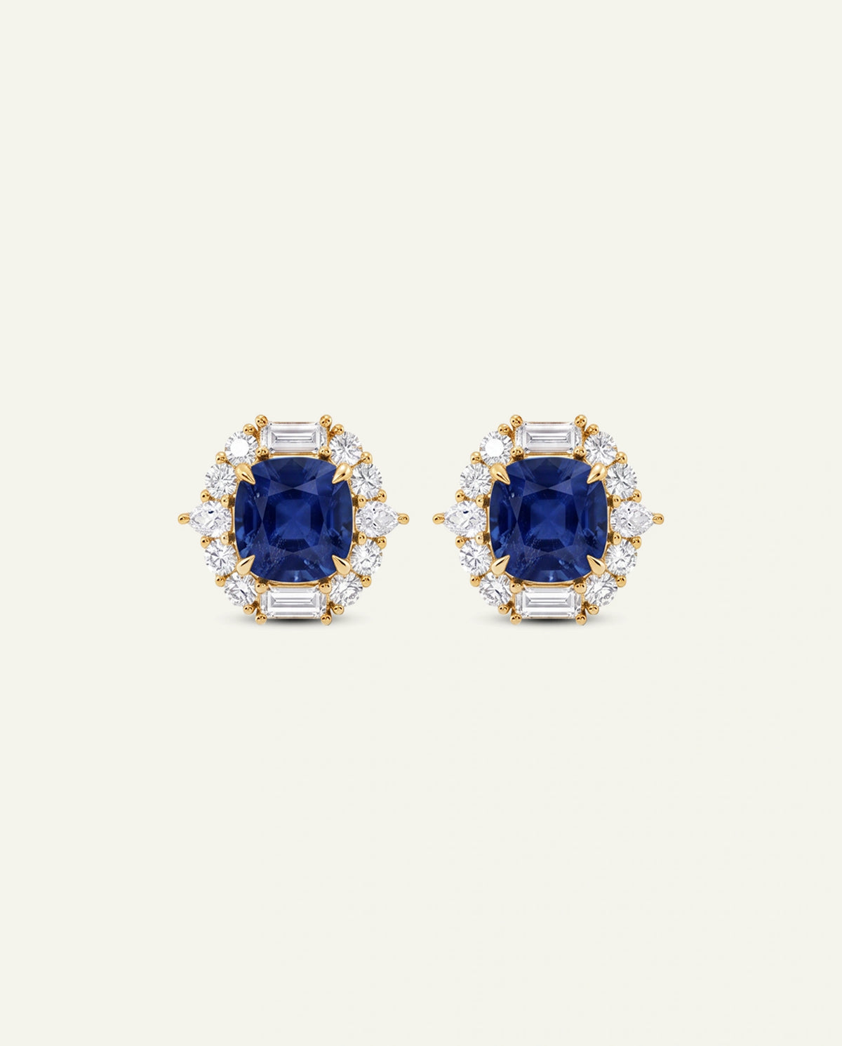 A pair of yellow gold stud earrings featuring a central cushion-cut blue sapphire surrounded by a halo of round and baguette-cut clear stones, set against a solid off-white background.