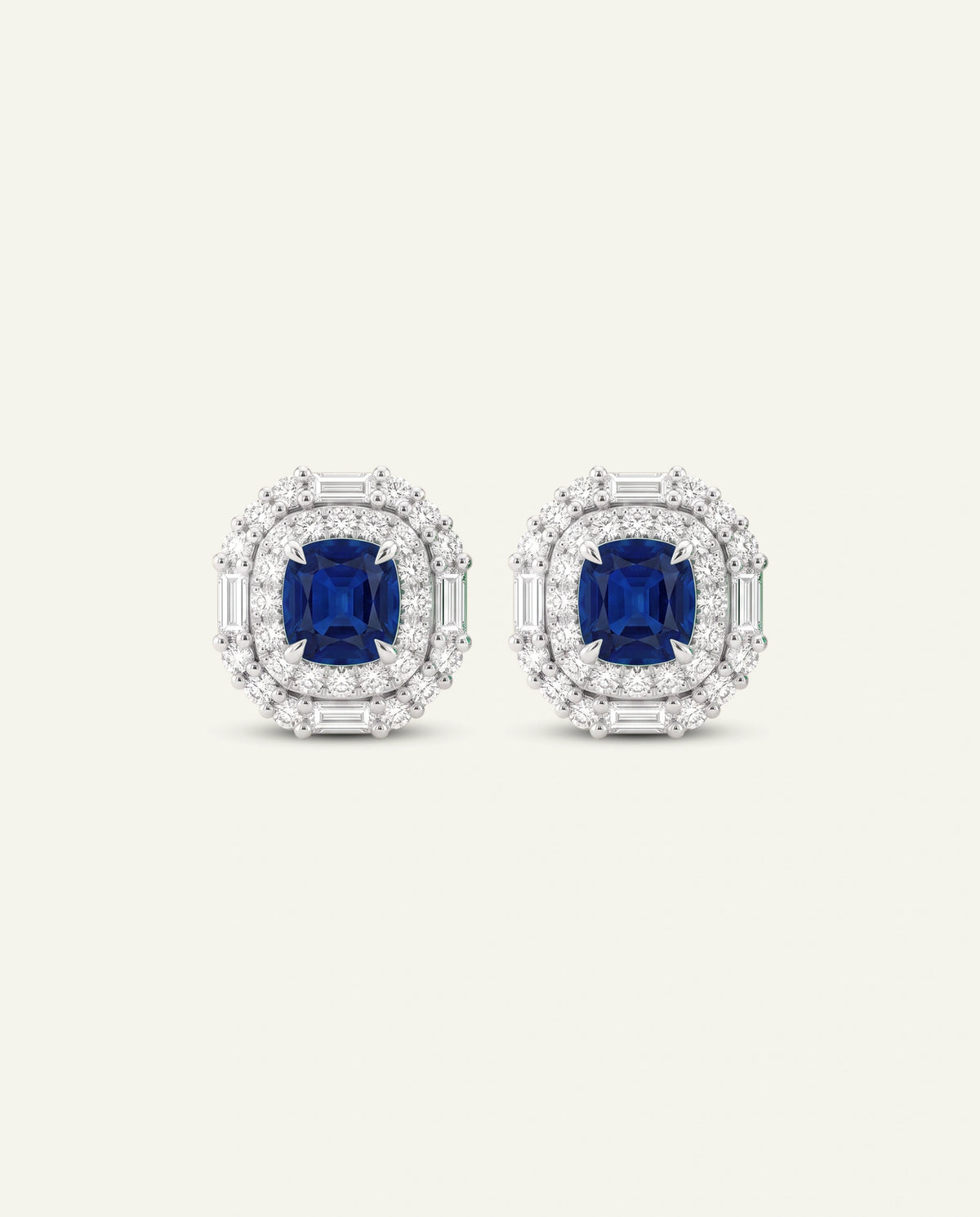 A pair of oval stud earrings featuring a central emerald-cut blue sapphire surrounded by a halo of small clear stones and baguette-cut side stones, set in a silver-toned metal on a light cream background.