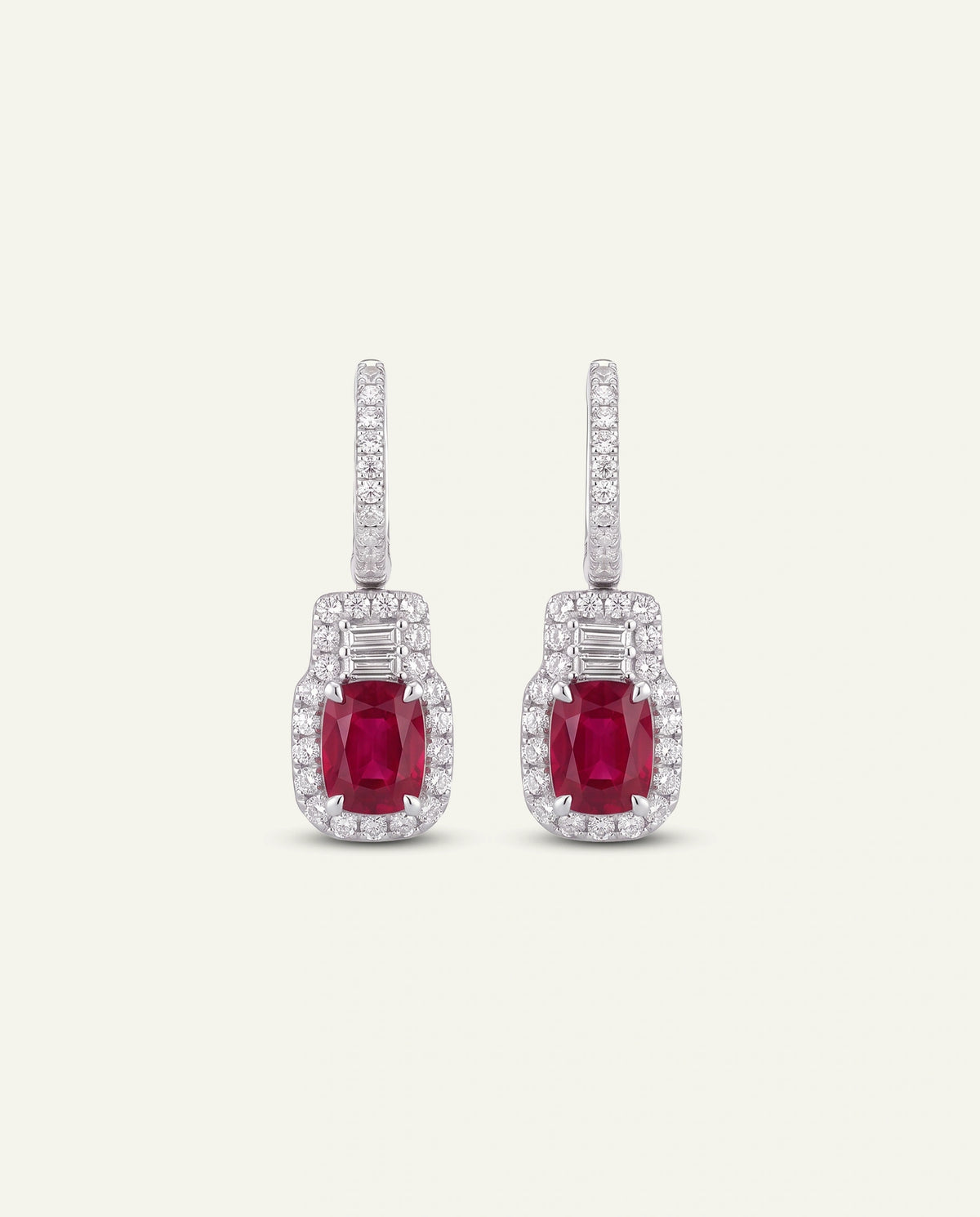 A pair of silver-tone drop earrings featuring rectangular emerald-cut ruby centers surrounded by small clear stones, with vertical rows of clear stones above, shown on a light cream background.