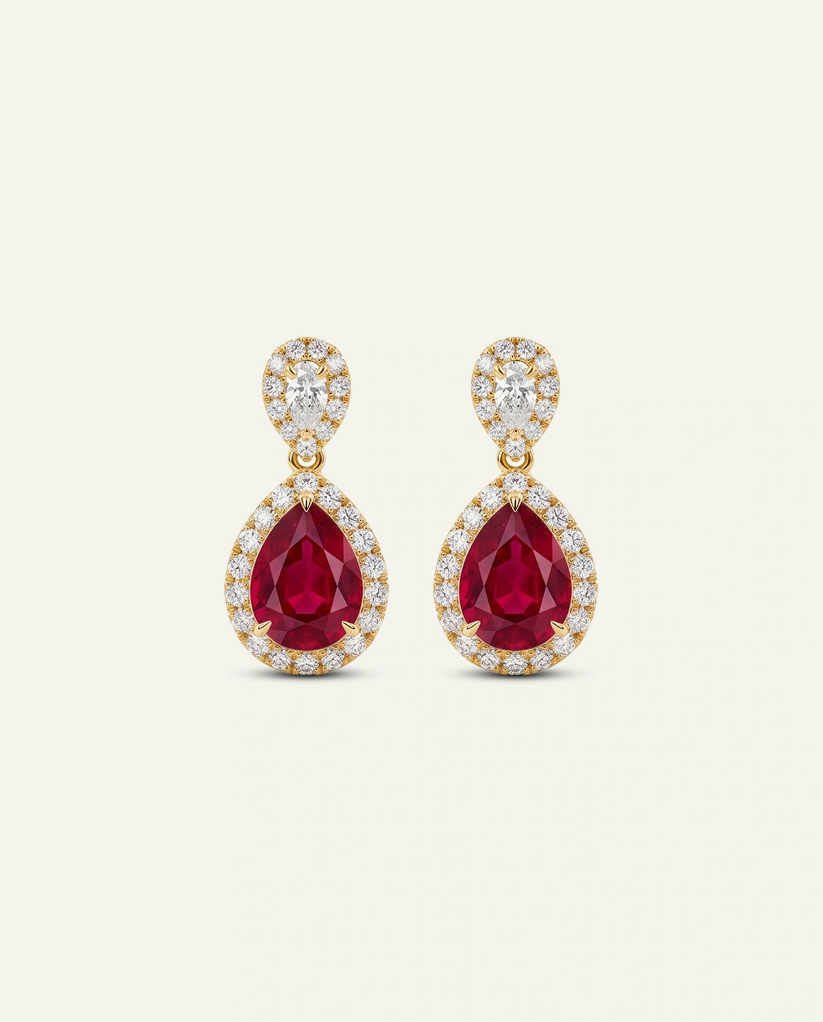 A pair of gold drop earrings featuring pear-shaped deep red gemstones surrounded by small clear stones, set against a plain off-white background.