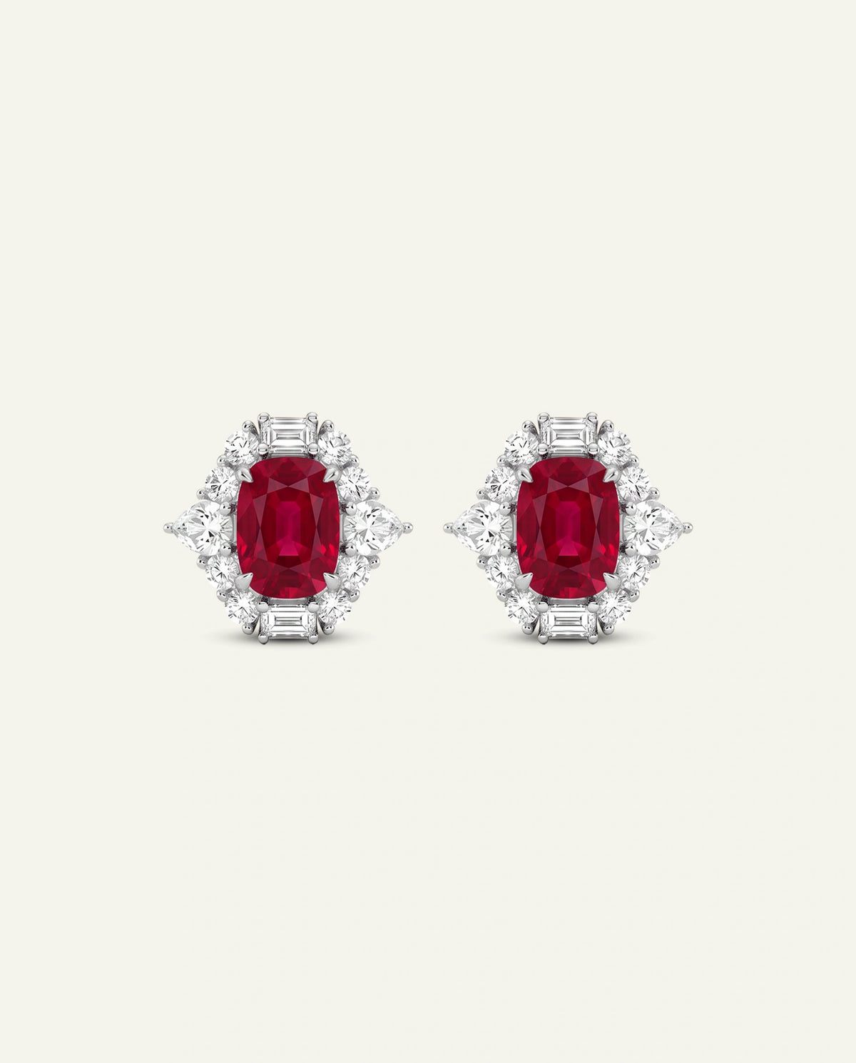 A pair of oval-cut red gemstone stud earrings surrounded by clear baguette and round-cut stones in a silver-toned setting, shown on a light cream background.