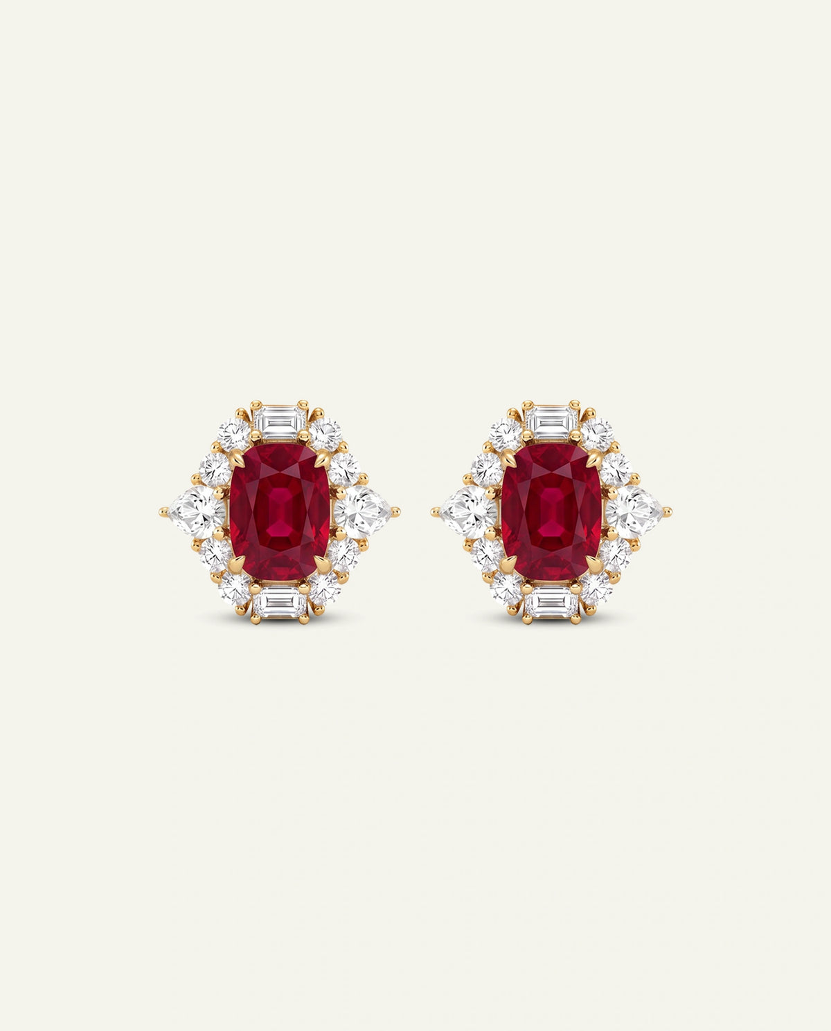 A pair of yellow gold stud earrings featuring oval-cut deep red rubies surrounded by small baguette-cut clear stones, set against a solid off-white background.