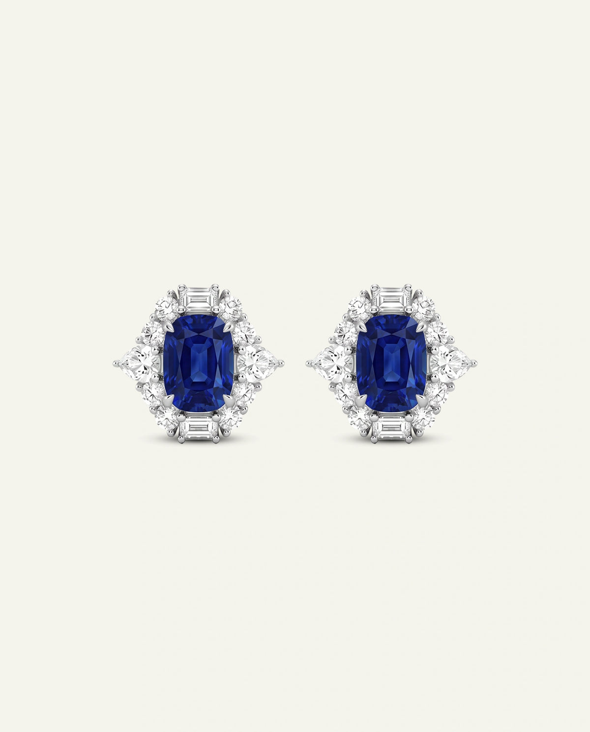 A pair of stud earrings featuring rectangular emerald-cut blue sapphires surrounded by small clear baguette and round-cut stones in a silver-toned setting, presented on a light cream background.