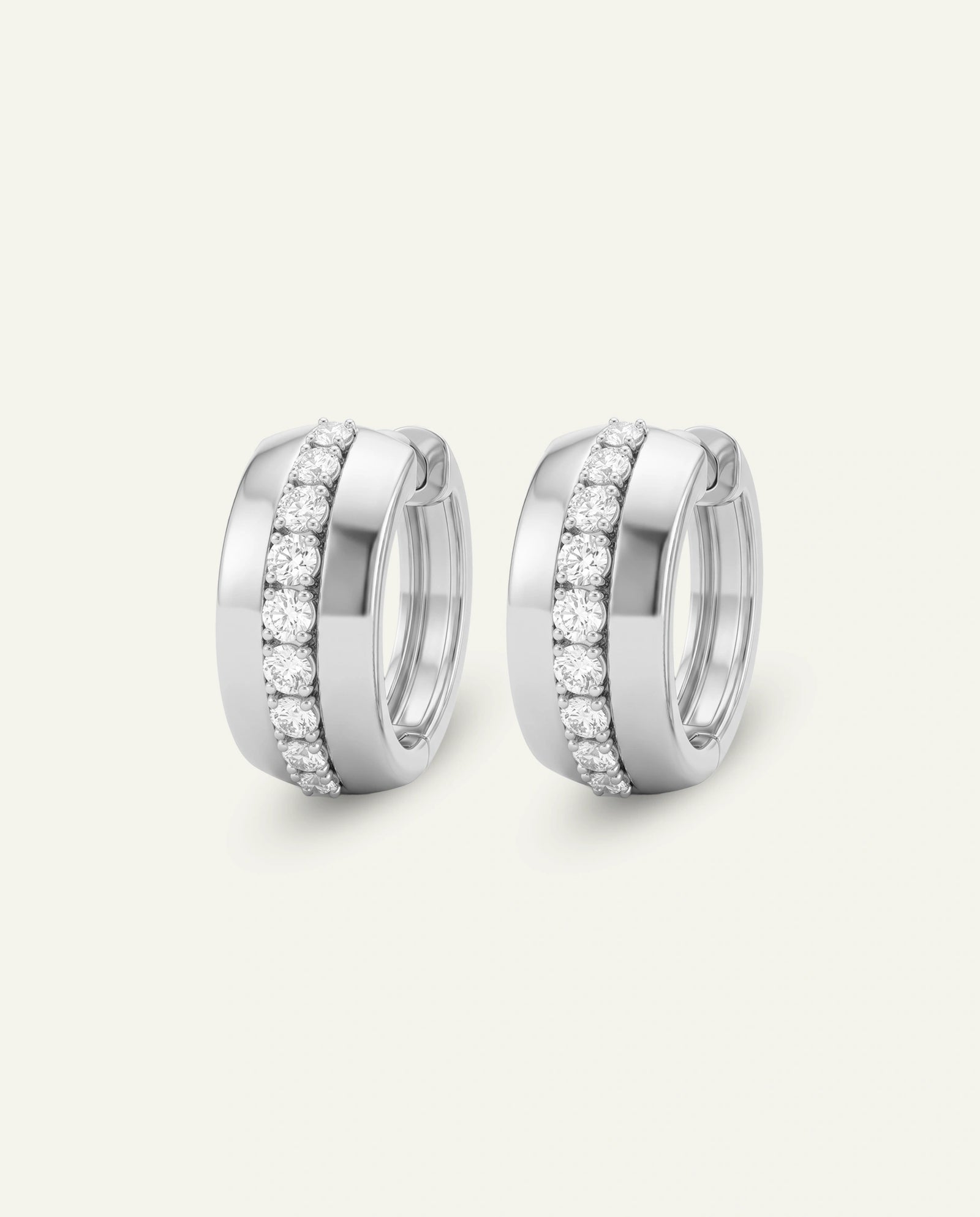 A pair of silver-toned huggie hoop earrings with pavé-set clear stones, shown on a light cream background.