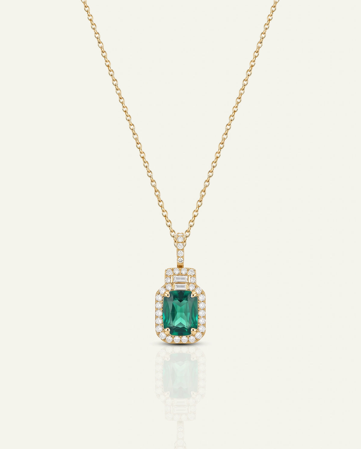 A gold necklace with a rectangular emerald-cut green gemstone pendant, surrounded by small clear stones, shown on a light cream background with a soft reflection below.