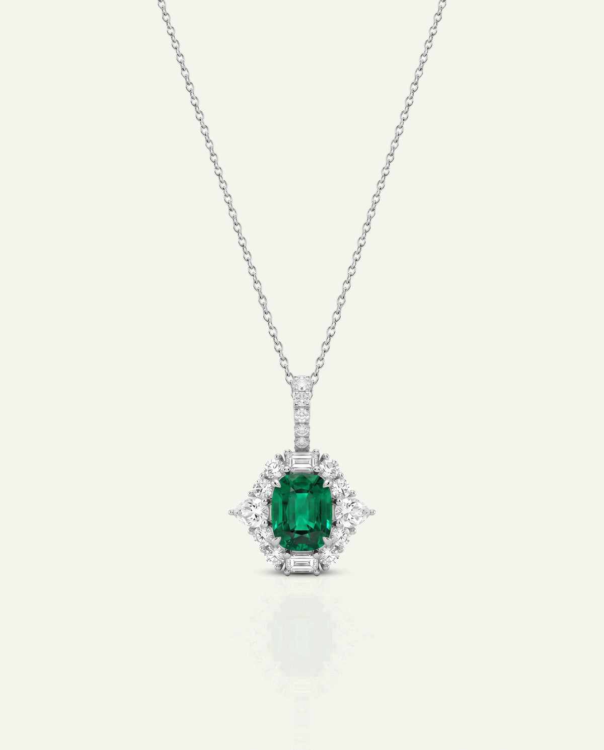 A silver pendant necklace featuring a central emerald-cut green gemstone surrounded by a halo of small clear stones, suspended from a delicate silver chain against a light cream background.