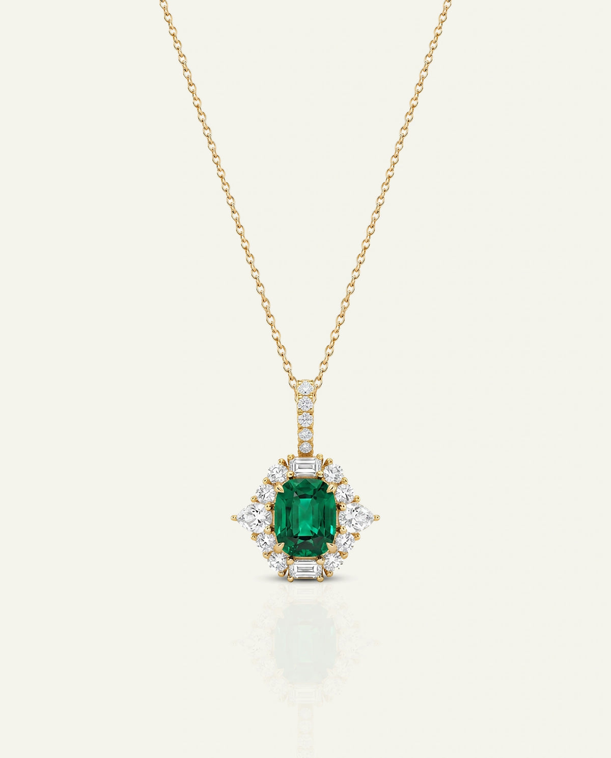 A gold necklace with a pendant featuring a rectangular emerald-cut green gemstone surrounded by small clear stones, shown on a light cream background.