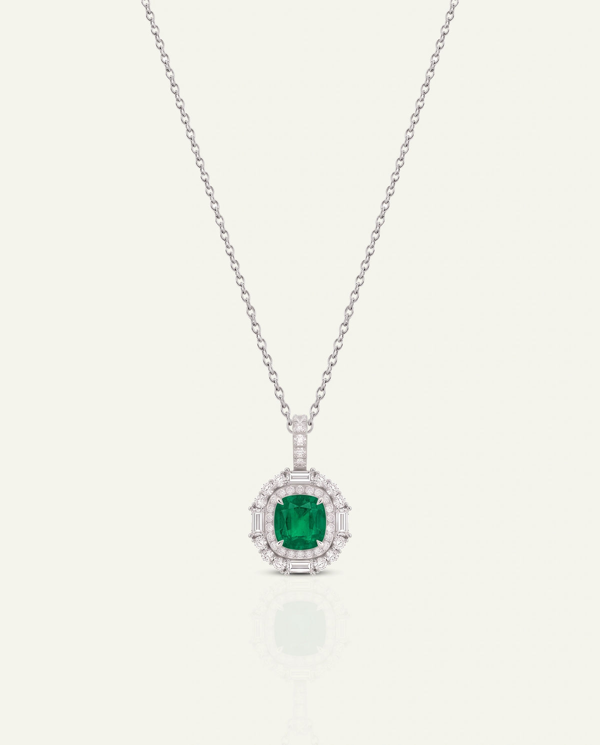 A silver-toned necklace with a round-cut green emerald pendant, surrounded by a halo of small clear stones, displayed on a light cream background.
