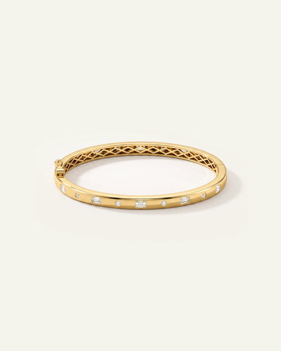 A gold hinged bangle bracelet with a diamond-encrusted outer band and an openwork lattice pattern on the inner band, shown on a light cream background.