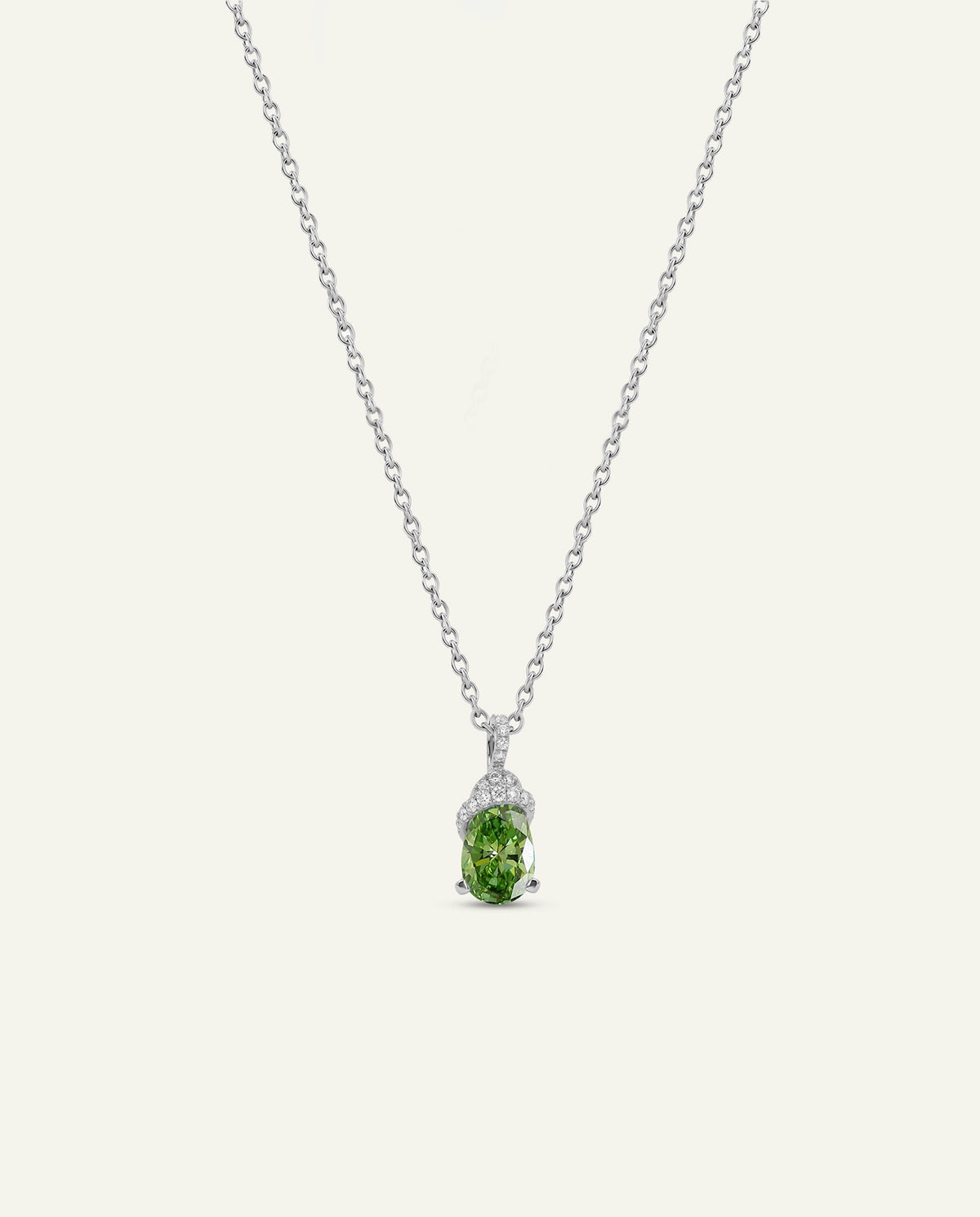 A delicate silver chain necklace featuring a pendant with a green oval gemstone and small clear accent stones, displayed against a light cream background.