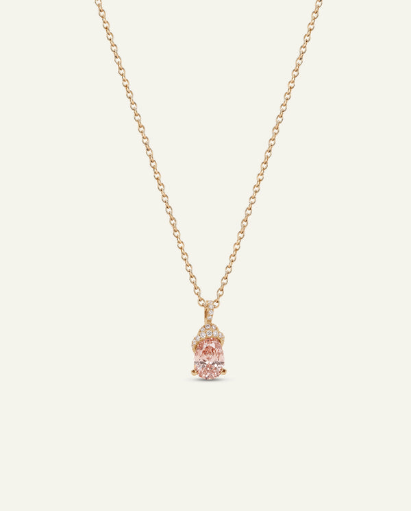 A delicate rose gold chain necklace featuring a small pendant with a central light pink gemstone and tiny clear accent stones, displayed against a solid off-white background.