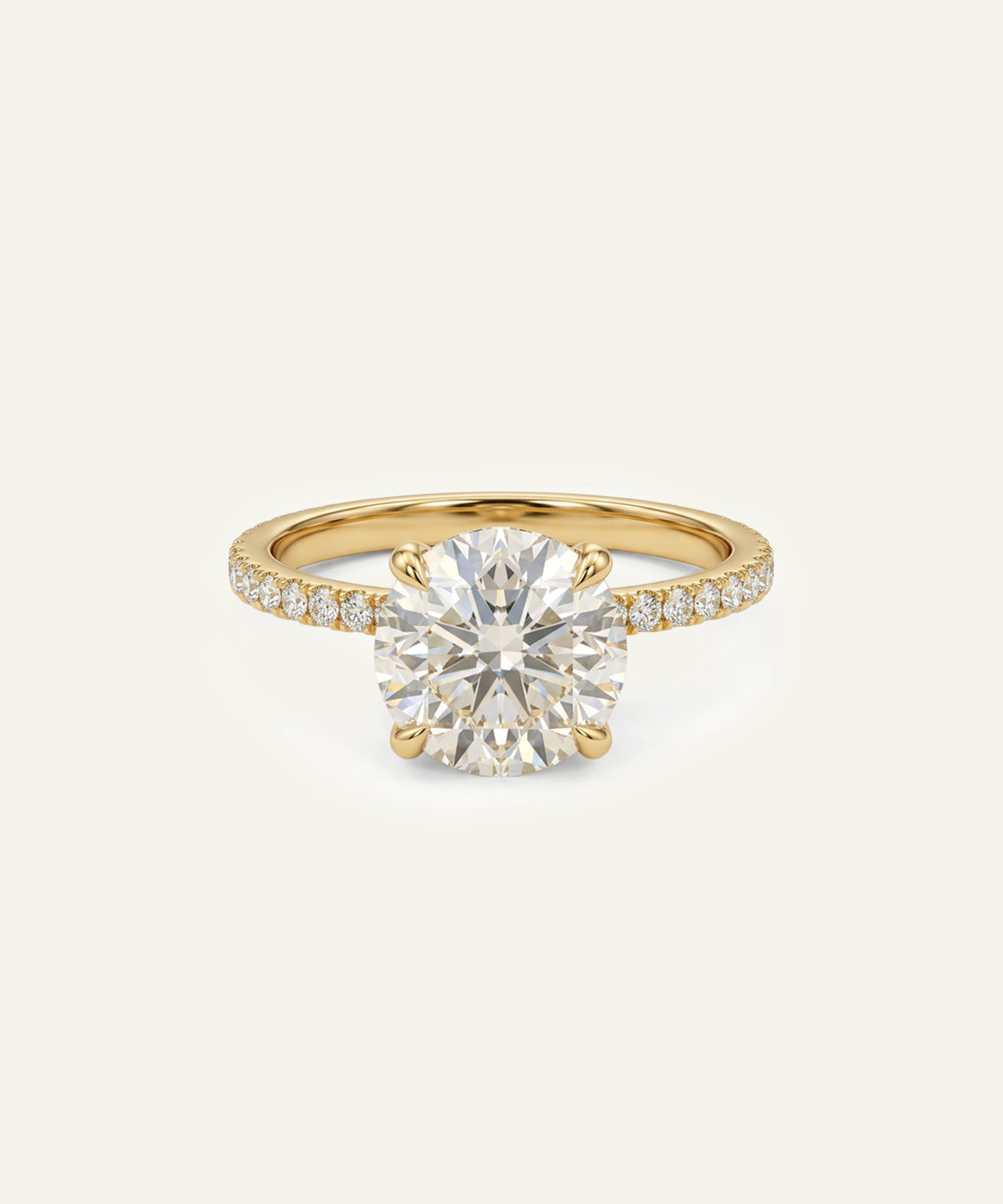 A yellow gold solitaire engagement ring featuring a round brilliant-cut diamond center stone and pavé-set diamonds along the shank, presented on a light cream background.