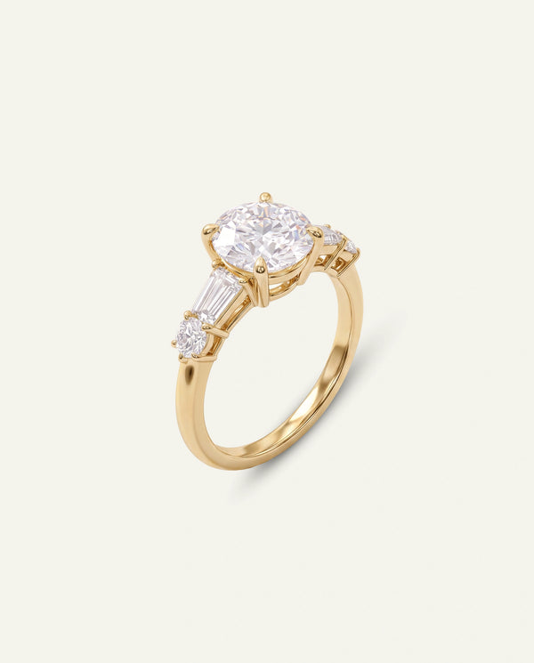 A yellow gold ring featuring a large oval-cut clear center stone and two baguette-cut side stones, set on a light cream background.
