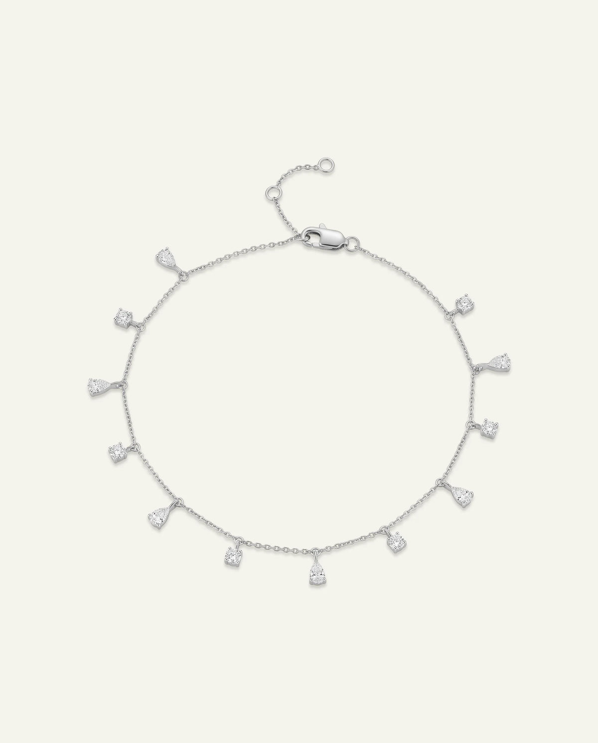 A delicate silver chain bracelet with multiple small teardrop-shaped clear gemstone drops, displayed on a light cream background.