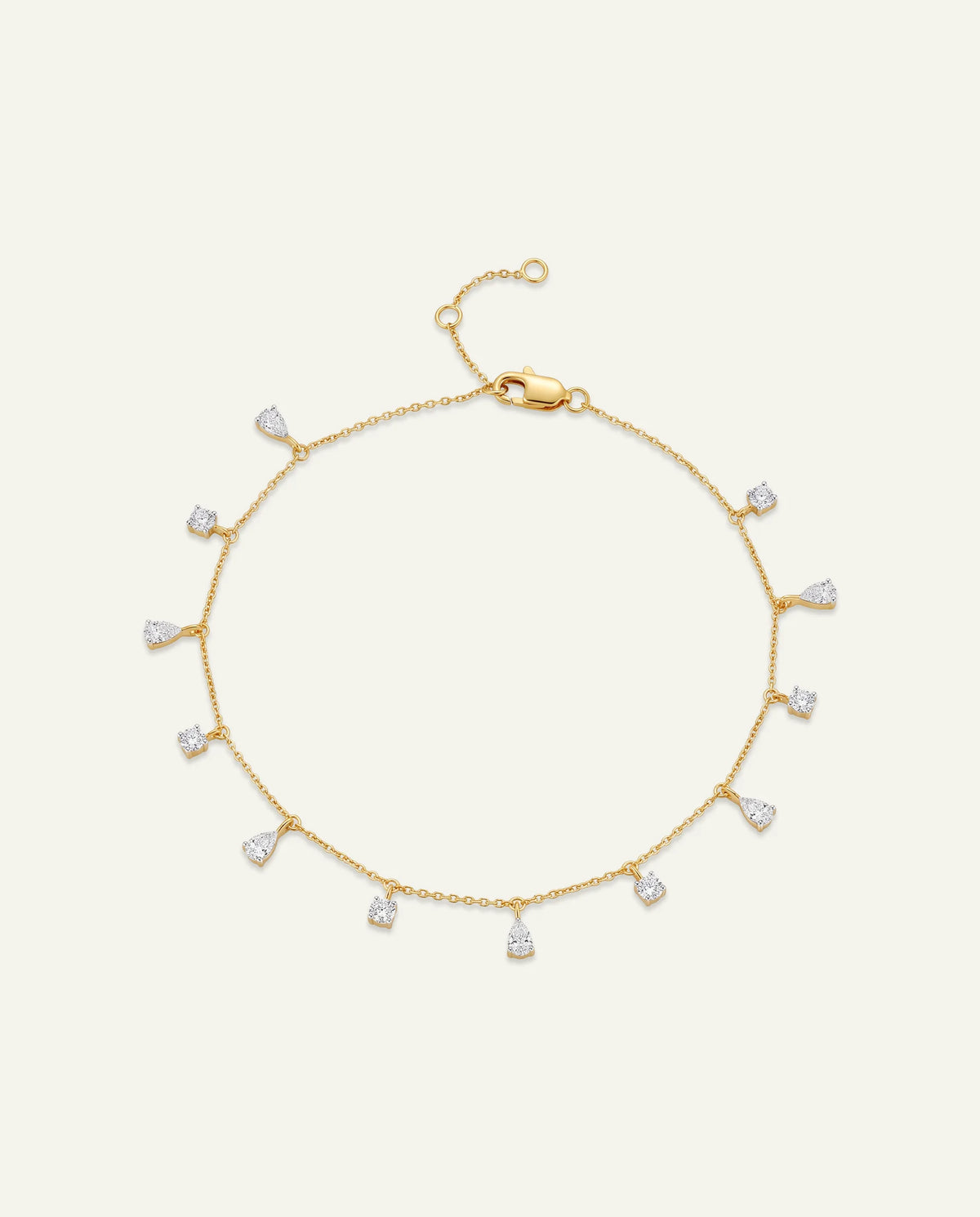 Yellow gold chain bracelet featuring dangling teardrop pear-cut diamond charms on an off-white background.