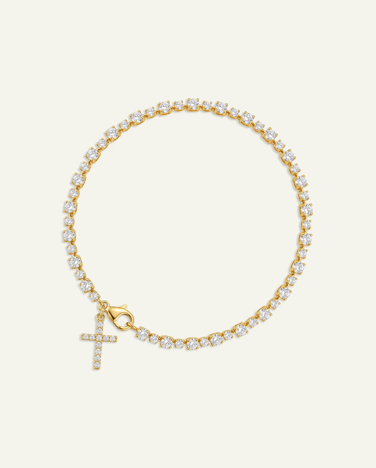 A delicate gold chain bracelet adorned with small clear stones and featuring a dangling cross charm, also embellished with stones, set against a solid off-white background.