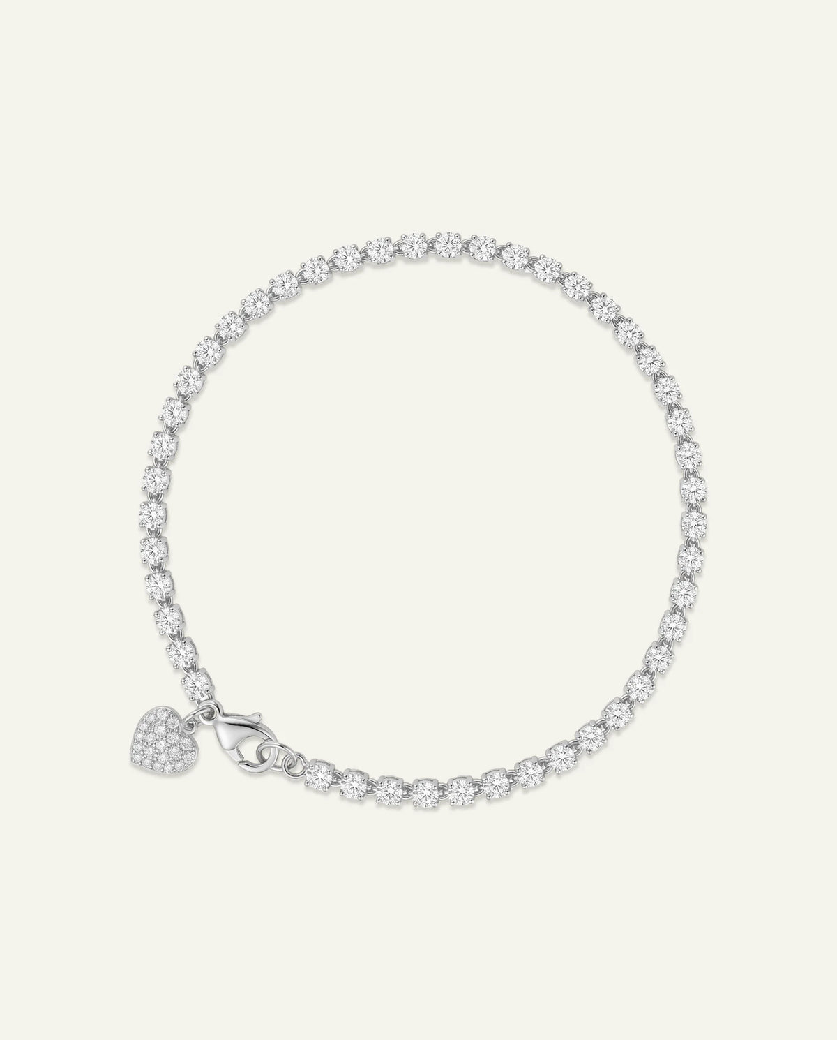 A silver tennis bracelet with a small heart-shaped pavé charm, displayed on a light cream background.
