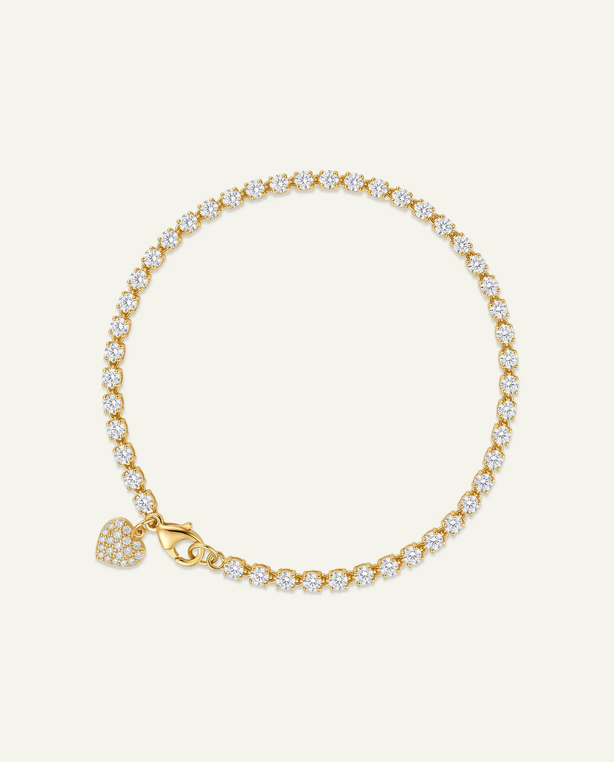 A gold tennis bracelet adorned with small clear pavé stones, featuring a heart-shaped pavé charm and a lobster clasp, displayed on a light cream background.