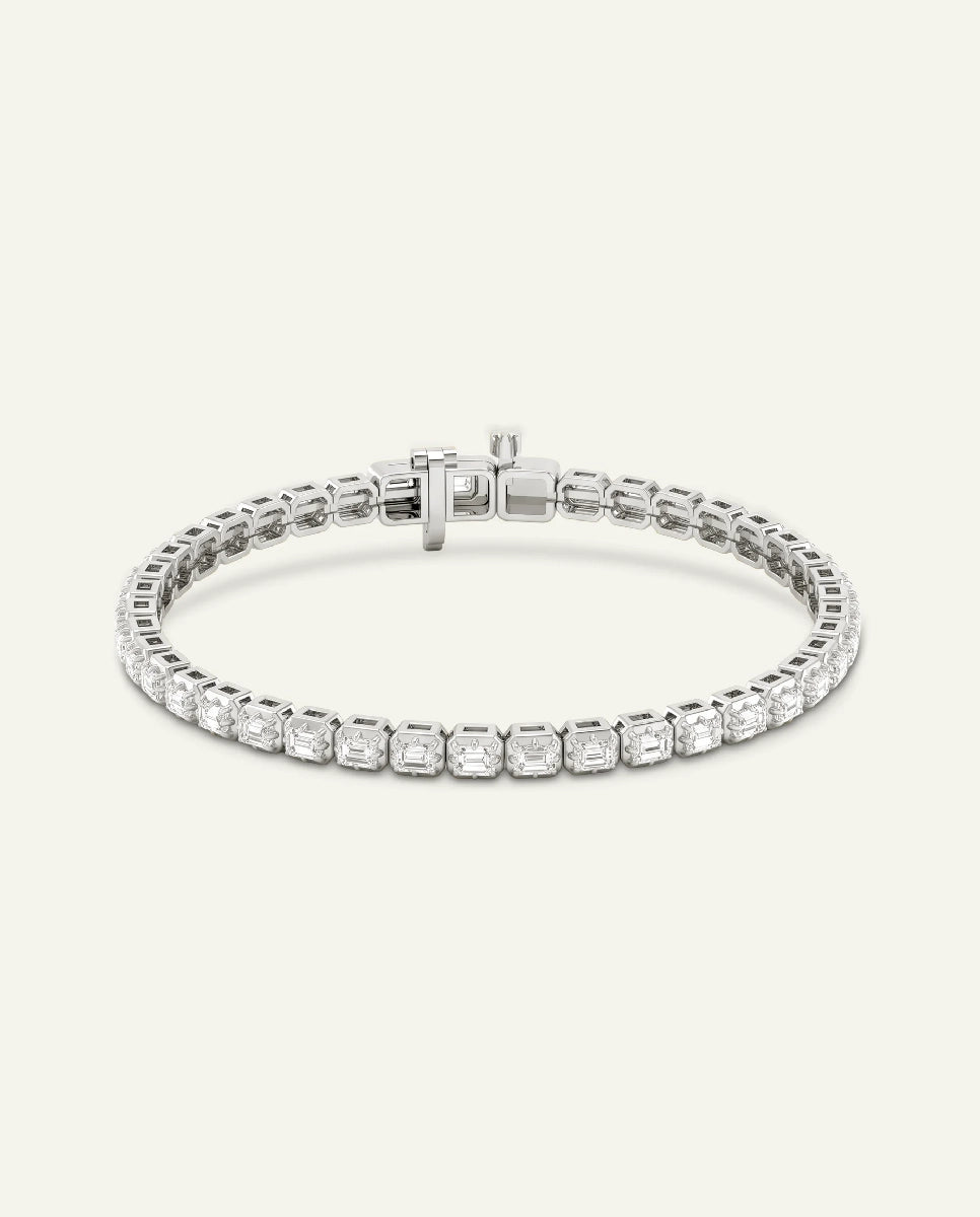 A silver tennis bracelet with a row of clear rectangular-cut stones, shown on a light cream background.