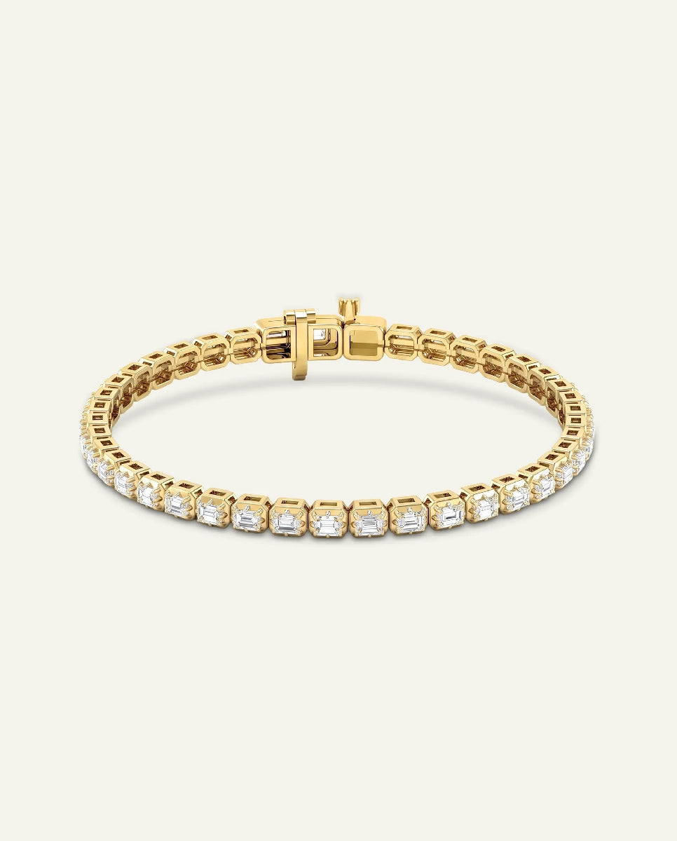 A gold tennis bracelet featuring a single row of clear square-cut gemstones in a bezel setting, displayed on a light cream background.
