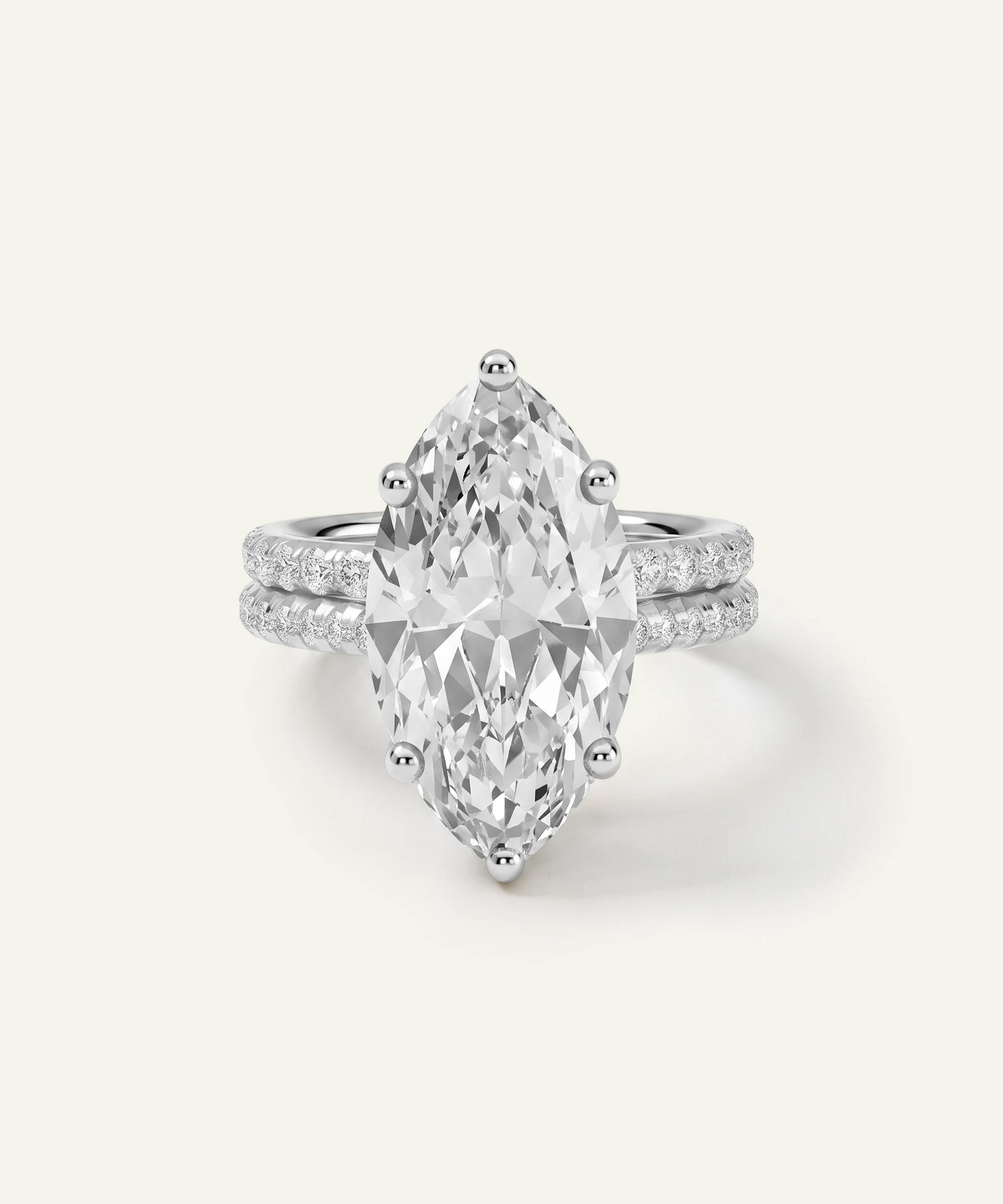A silver-tone ring featuring a large marquise-cut clear gemstone in a prong setting, with a double-row pavé band of smaller round stones, shown on a light cream background.