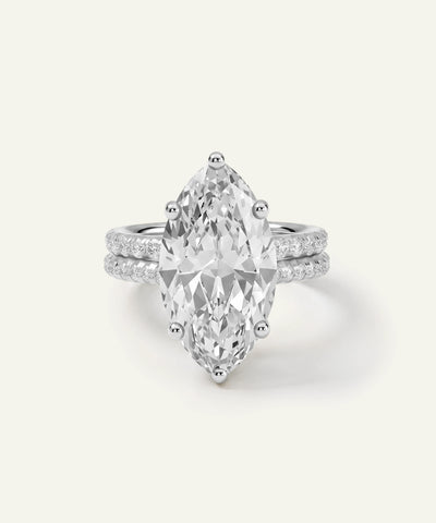 A silver-tone ring featuring a large marquise-cut clear gemstone in a prong setting, with a double-row pavé band of smaller round stones, shown on a light cream background. - alternate view