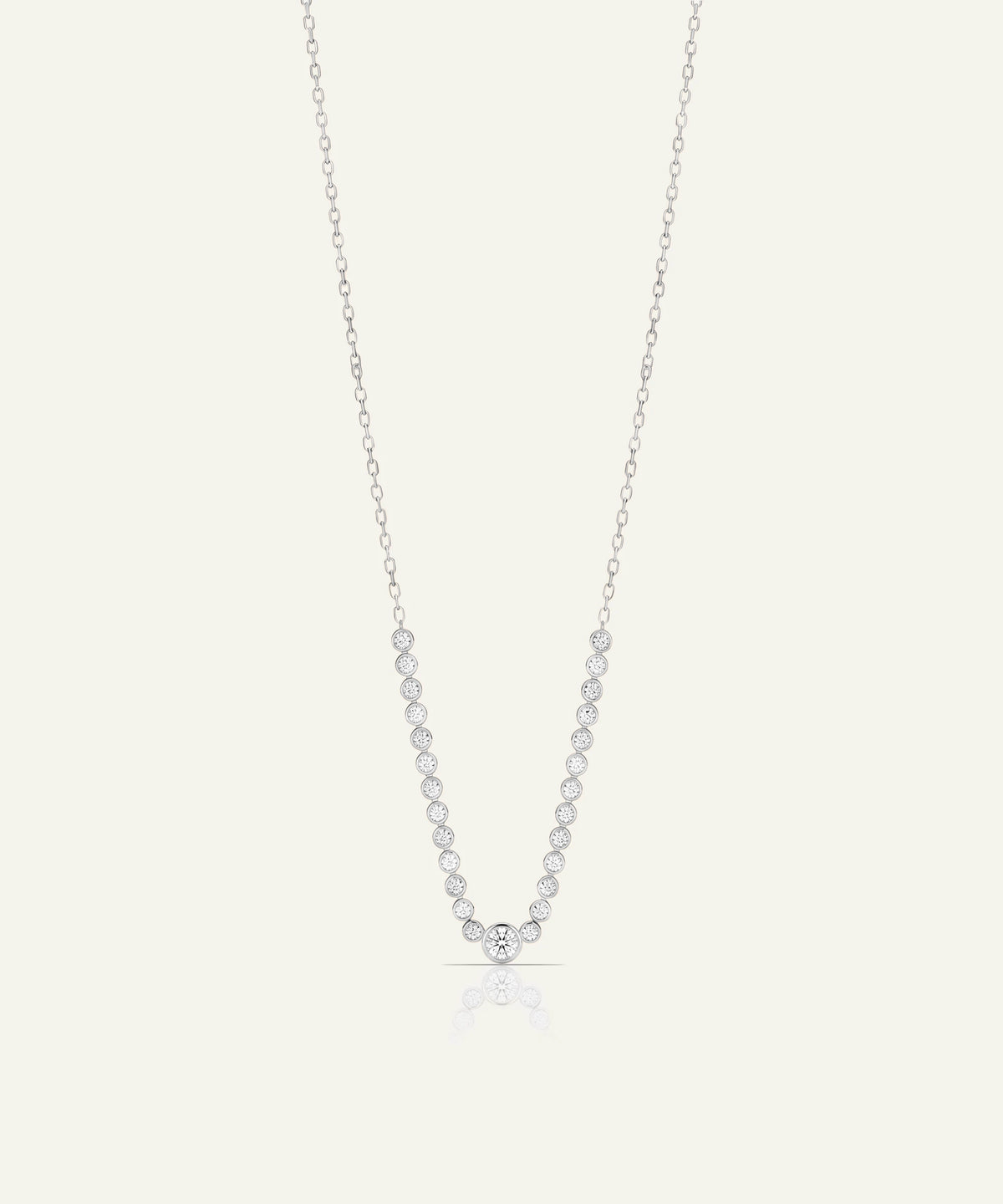 A delicate silver chain necklace featuring a V-shaped pendant set with small, clear round-cut gemstones, displayed against a solid off-white background.
