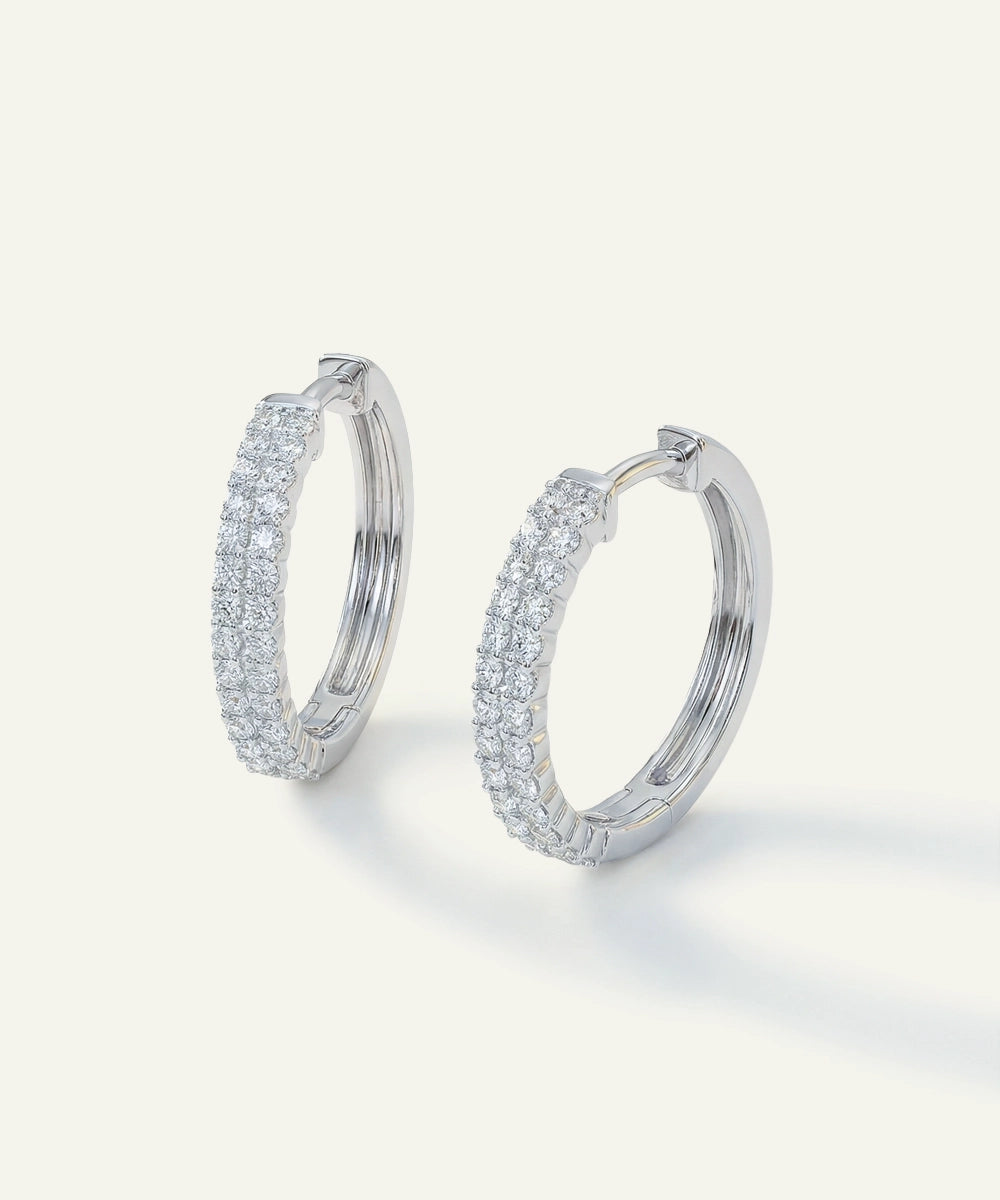 Pair of silver hoop earrings with clear gemstones on a light gray background