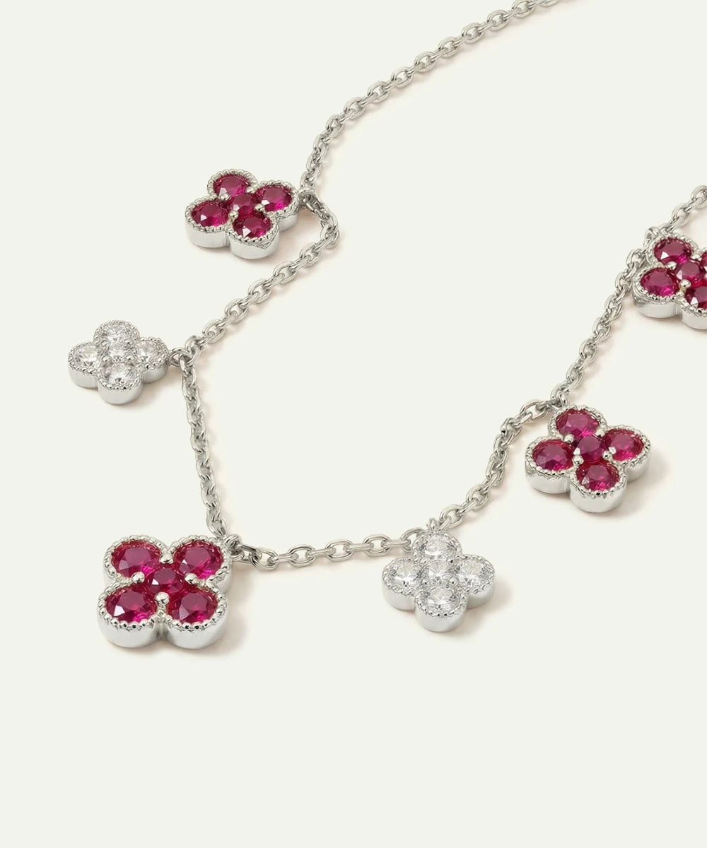 Silver necklace with flower-shaped pendants featuring red gemstones on a white background