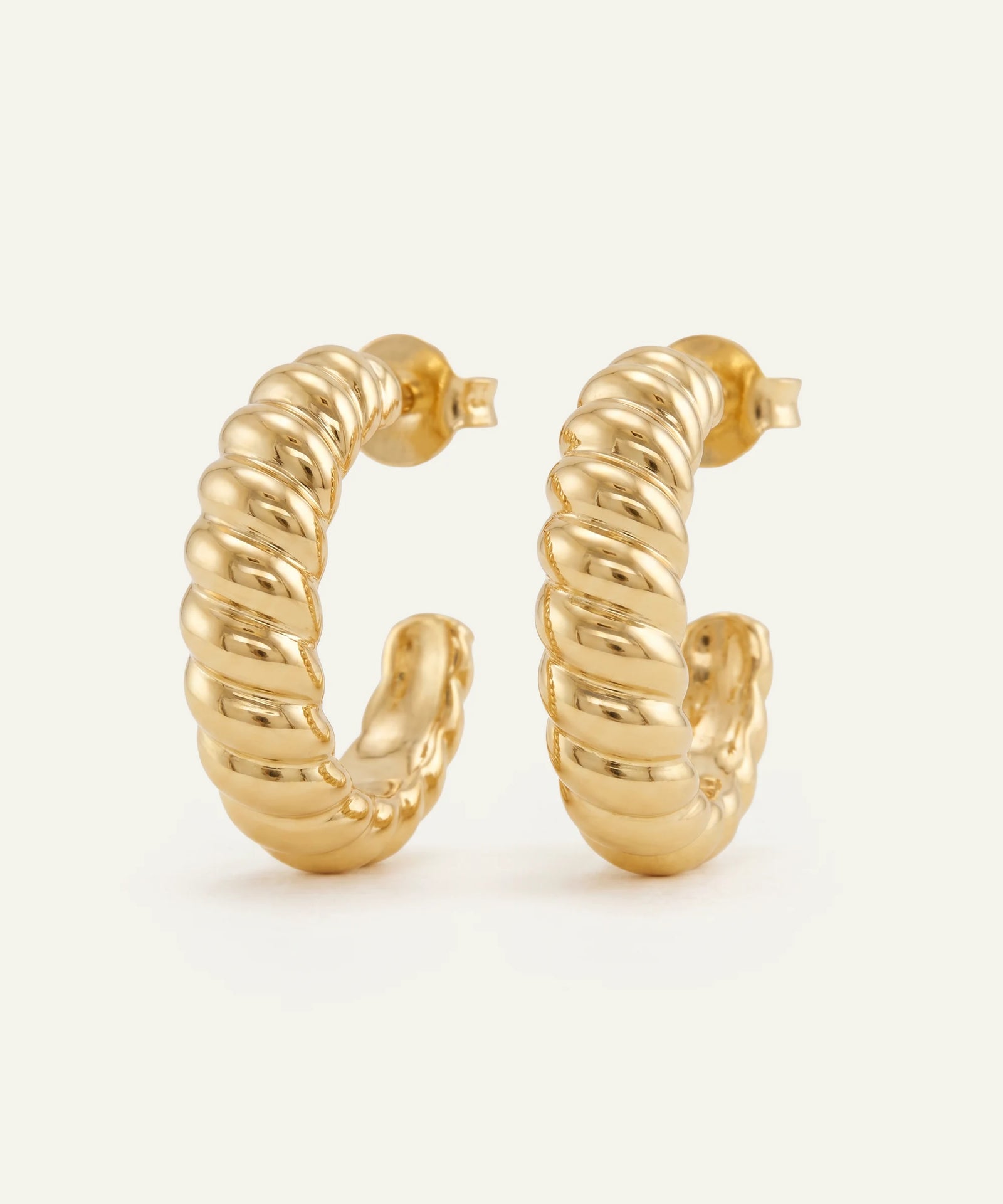 Gold hoop earrings with a ribbed texture on a light beige background