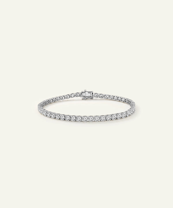 A silver tennis bracelet with a row of small round-cut stones and a rectangular center stone, displayed on a light cream background.
