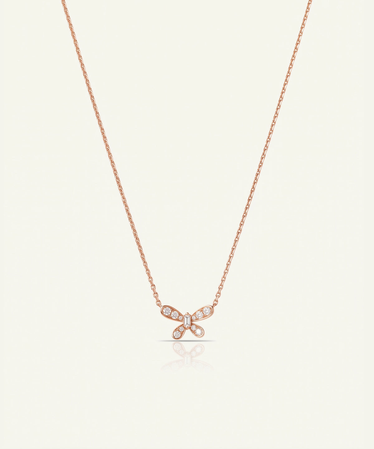 A delicate rose gold chain necklace featuring a small bow-shaped pendant paved with clear stones, displayed against a solid off-white background.