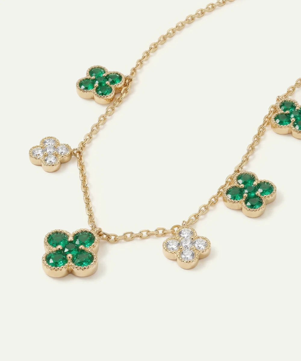Gold necklace with green gemstone clover pendants on a white background